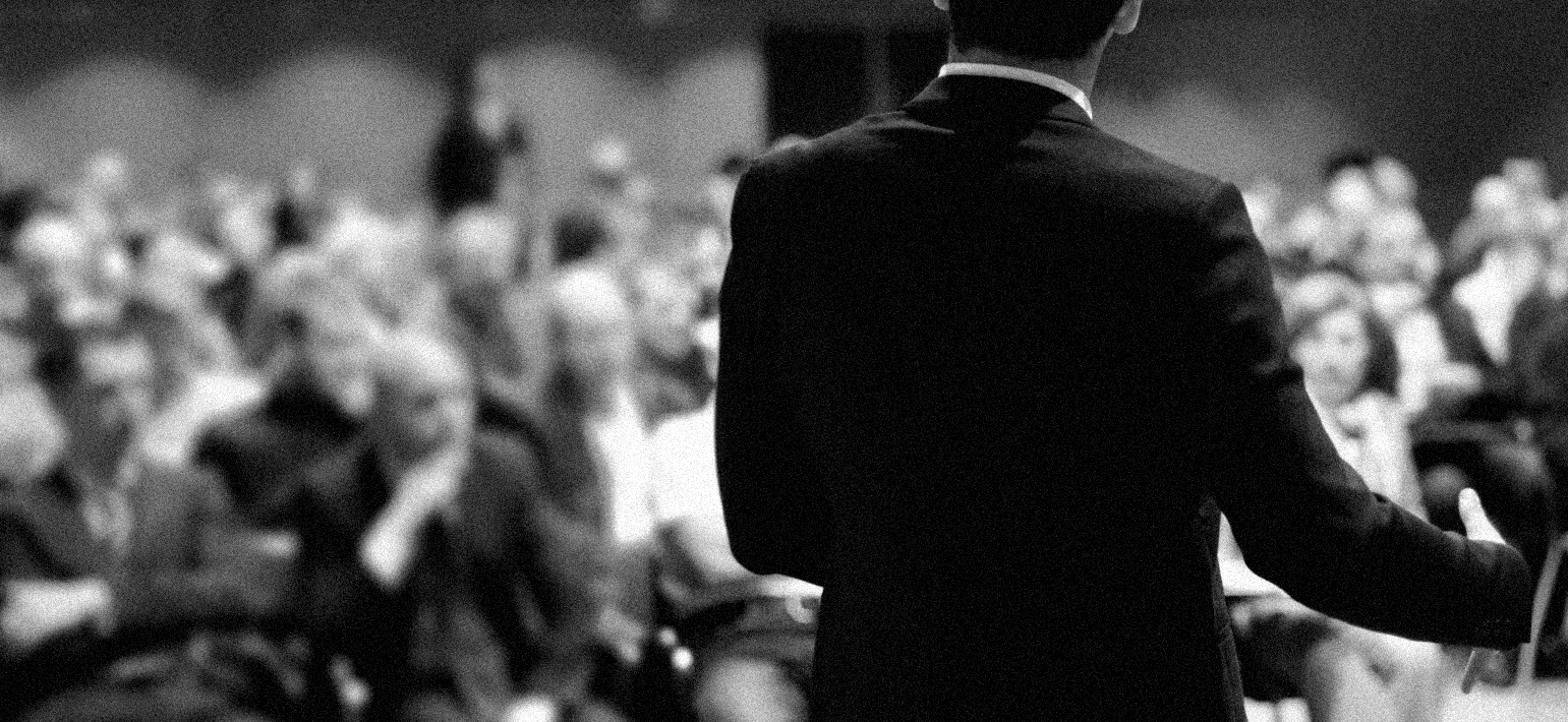 A consulting Person in a black suit doing consultations in front of an audience.